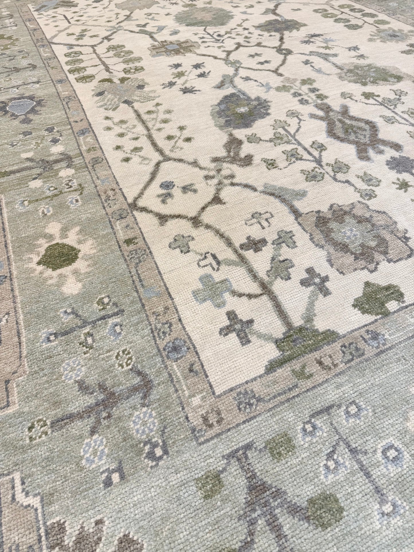 Close-up of a patterned blue and green Turkish Oushak rug with floral designs on a neutral background