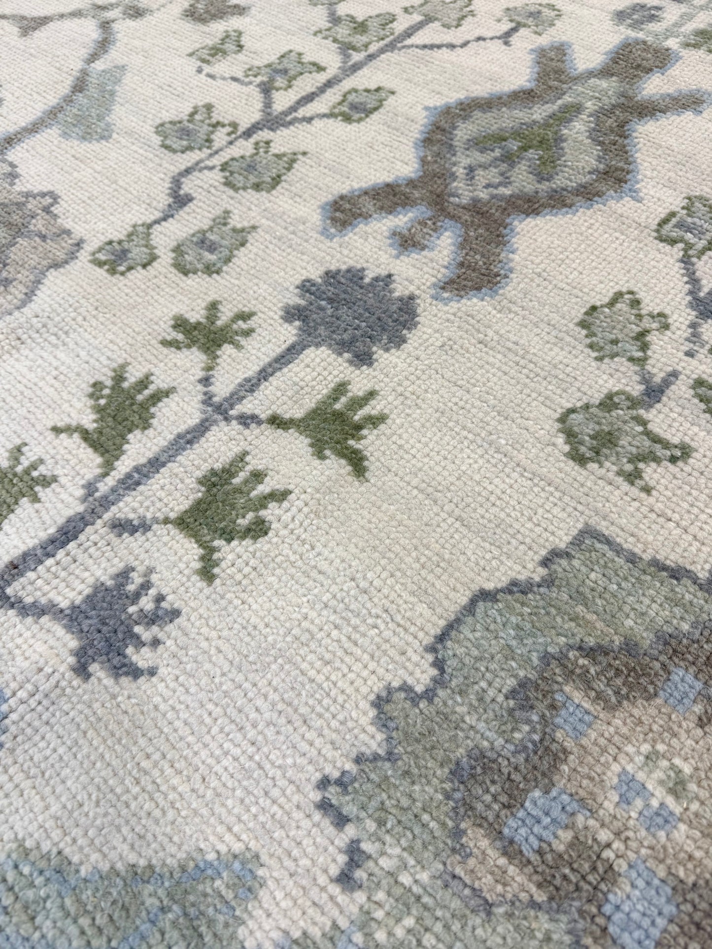 Close-up of a turkish oushak rug with green and blue designs on a beige background