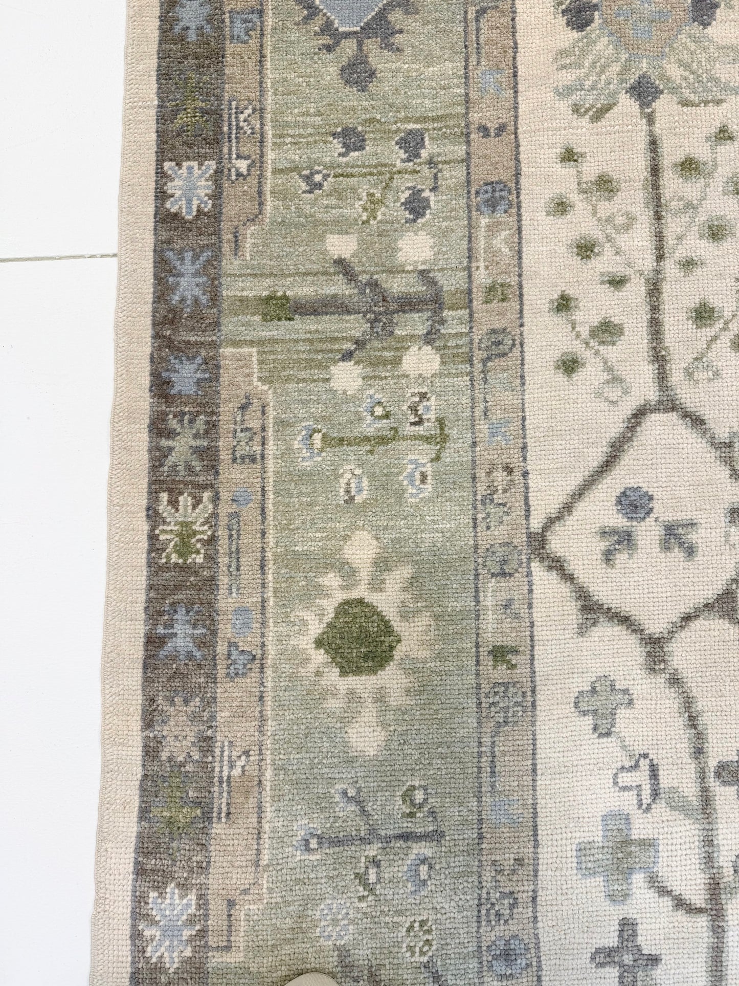 Close-up of Eden Turkish oushak rug with blues and greens with geometric designs on a neutral background