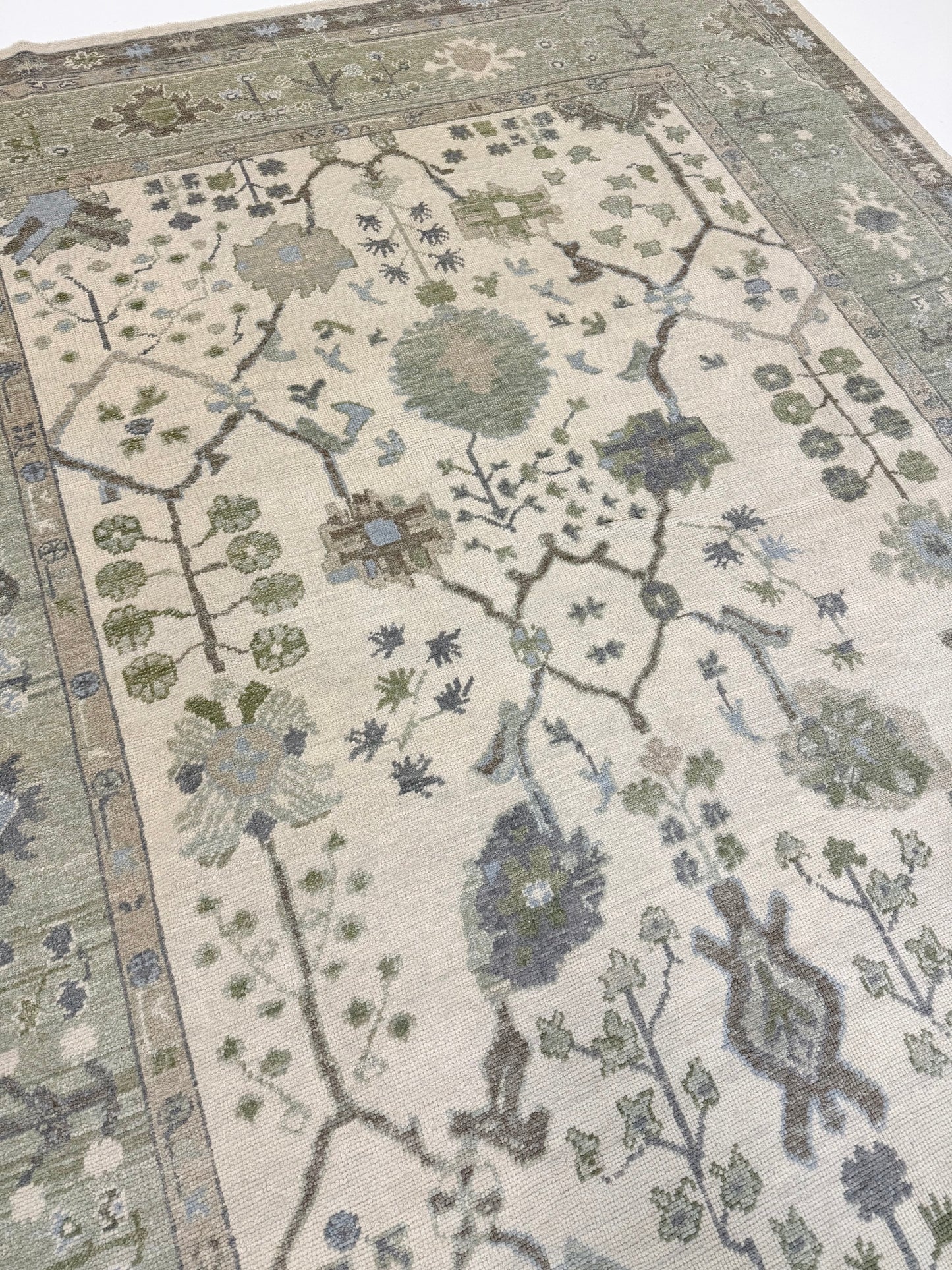 Turkish oushak rug with blues and greens and intricate patterns on a neutral background