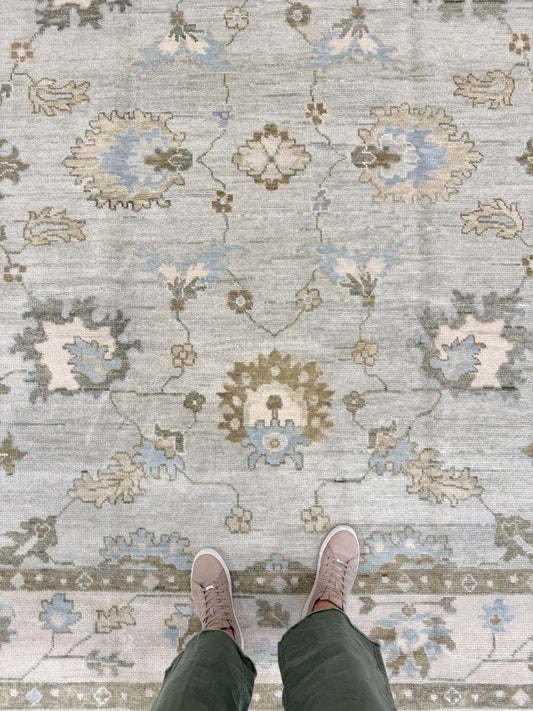 Person wearing mushroom colored shoes standing on a Sage Green Modern Oushak hand-knotted wool rug with blues, greens, creams and browns