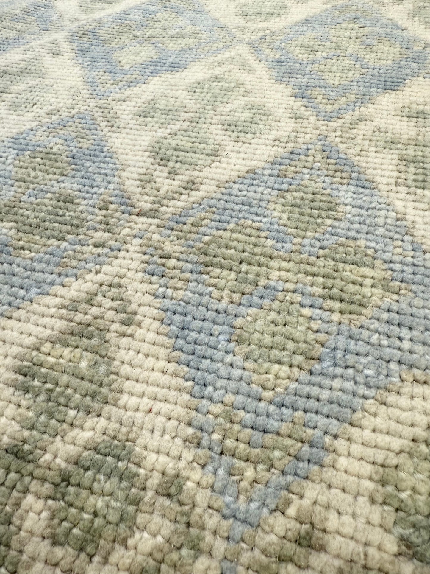 Close-up of hand-knotted turkish Oushak rug with a geometric pattern in shades of blue, green, and beige.