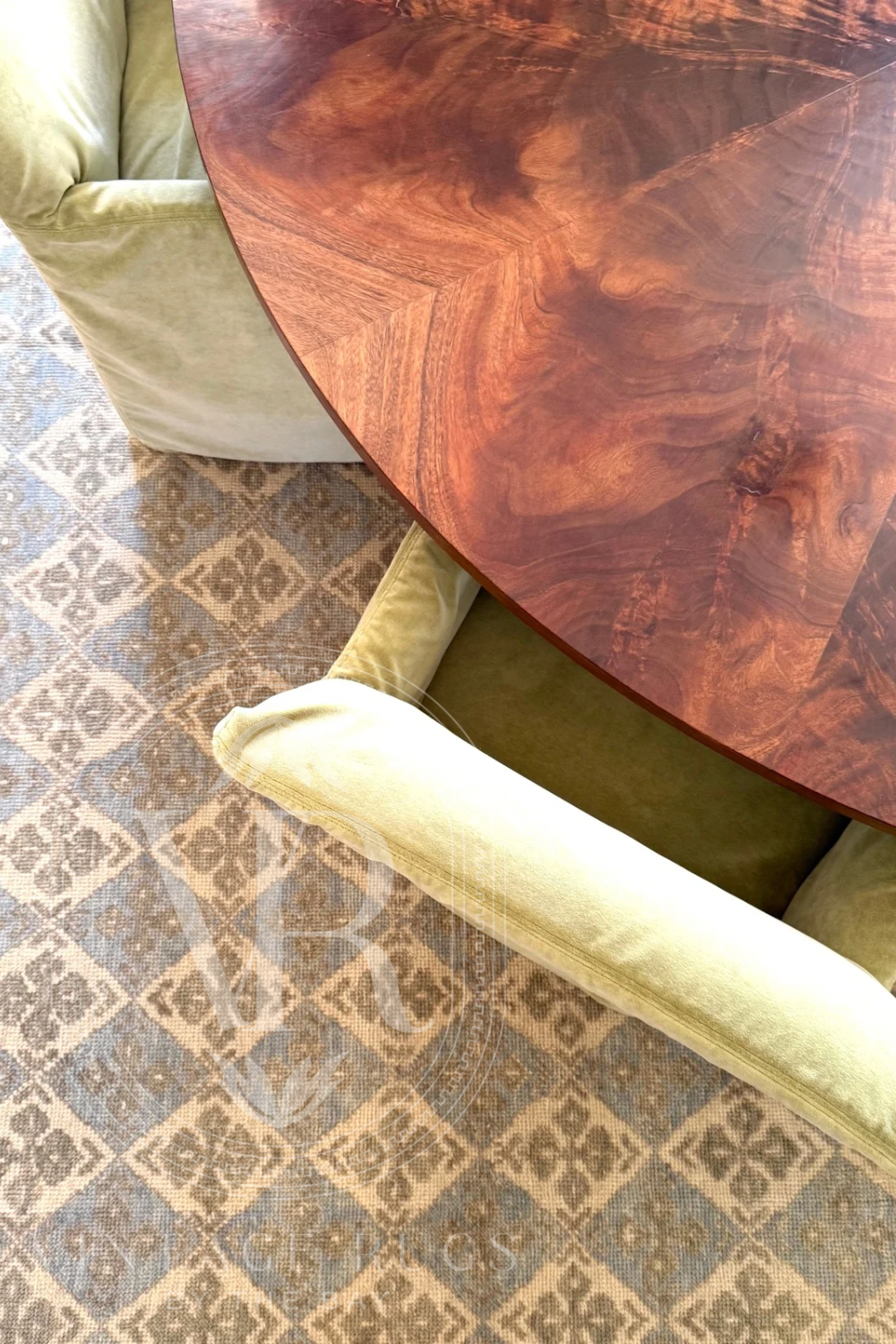 Round wooden table with a wool turkish oushak rug and green upholstered chairs.