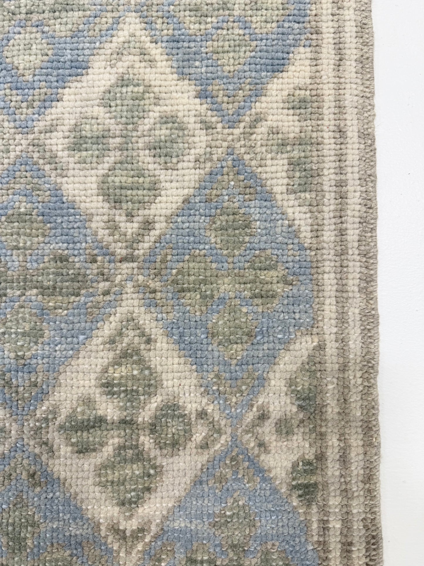 Close-up of a hand knotted Turkish oushak rug with geometric pattern in blue, gray, and white.