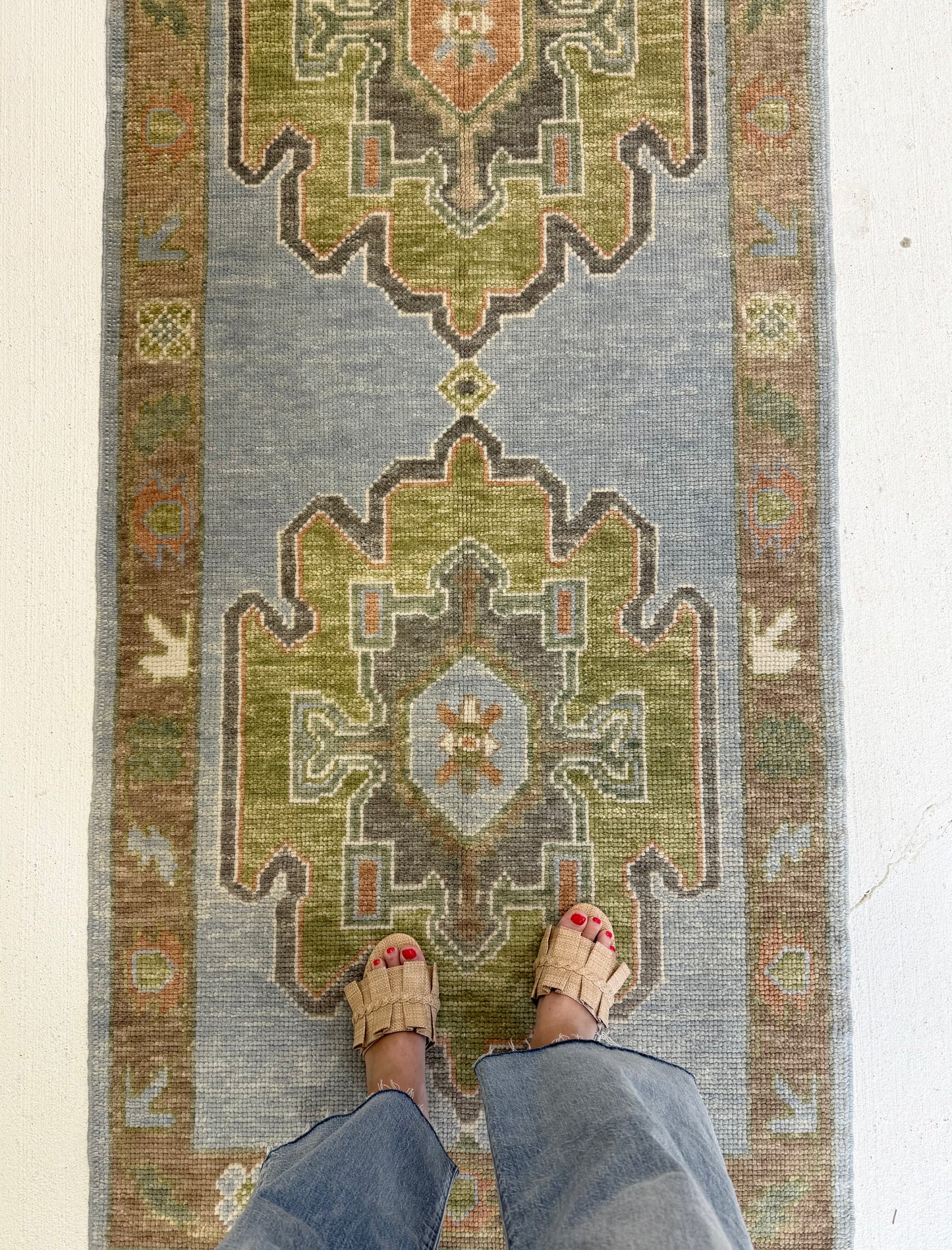 Person standing on a blue and green patterned turkish oushak hand-knotted rug with feet visible