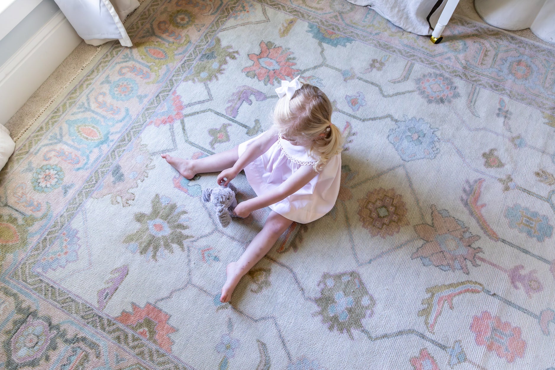 Young girl sitting atop a beautiful, durable hand-knotted modern Oushak rug with cream color, pink, green, coral in Alabama bedroom.