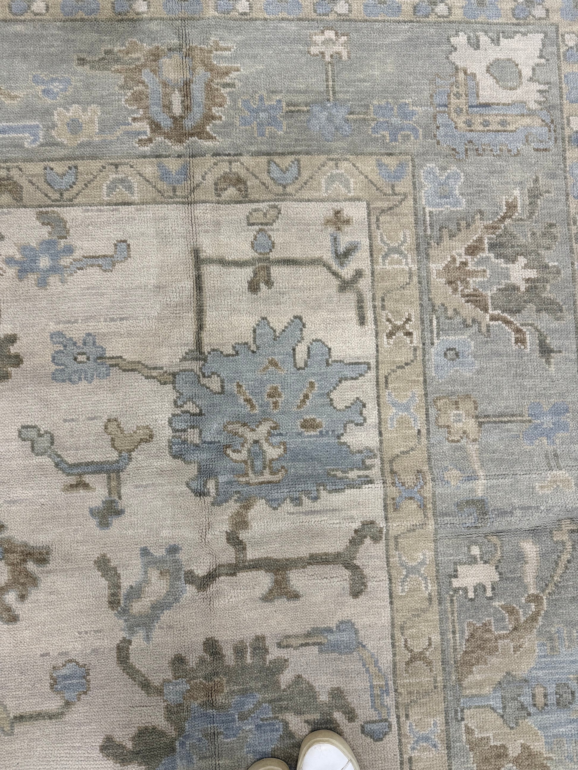 Close-up of warm modern oushak wool rug with intricate designs in gray, blue, and beige.