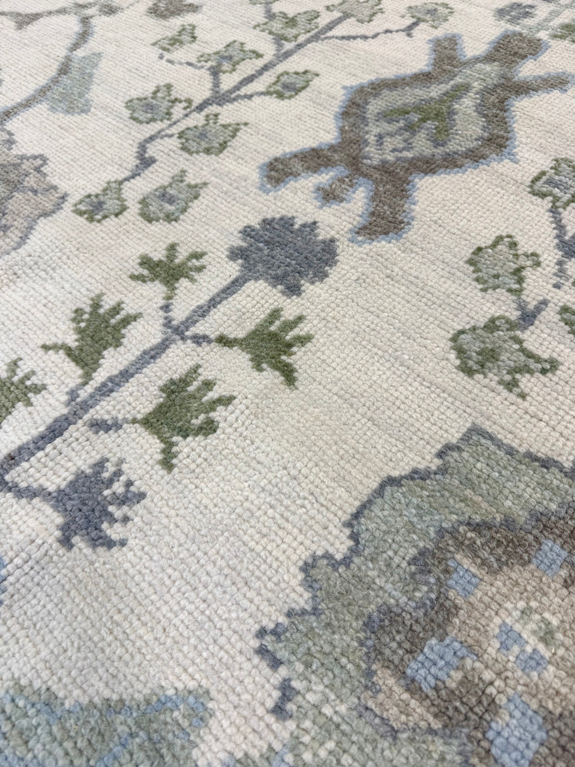 Close-up of a turkish oushak rug with green and blue designs on a beige background
