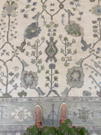 Close-up of a patterned  blue and green turkish oushak rug with floral designs on a neutral background.