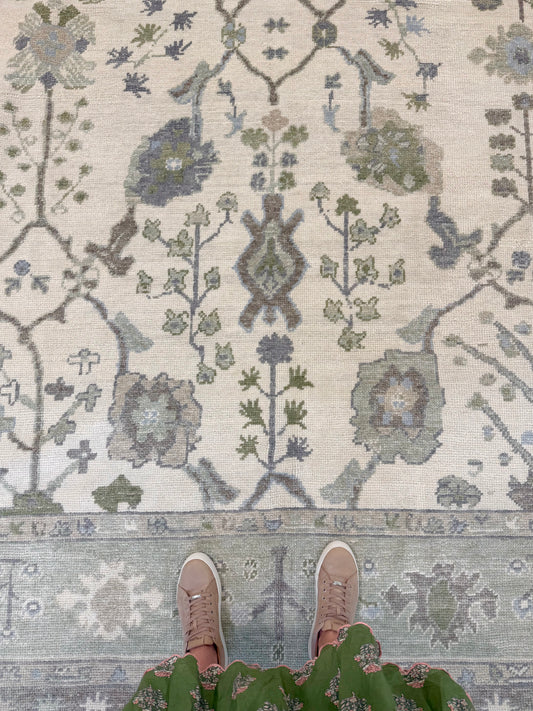 Close-up of a patterned  blue and green turkish oushak rug with floral designs on a neutral background.