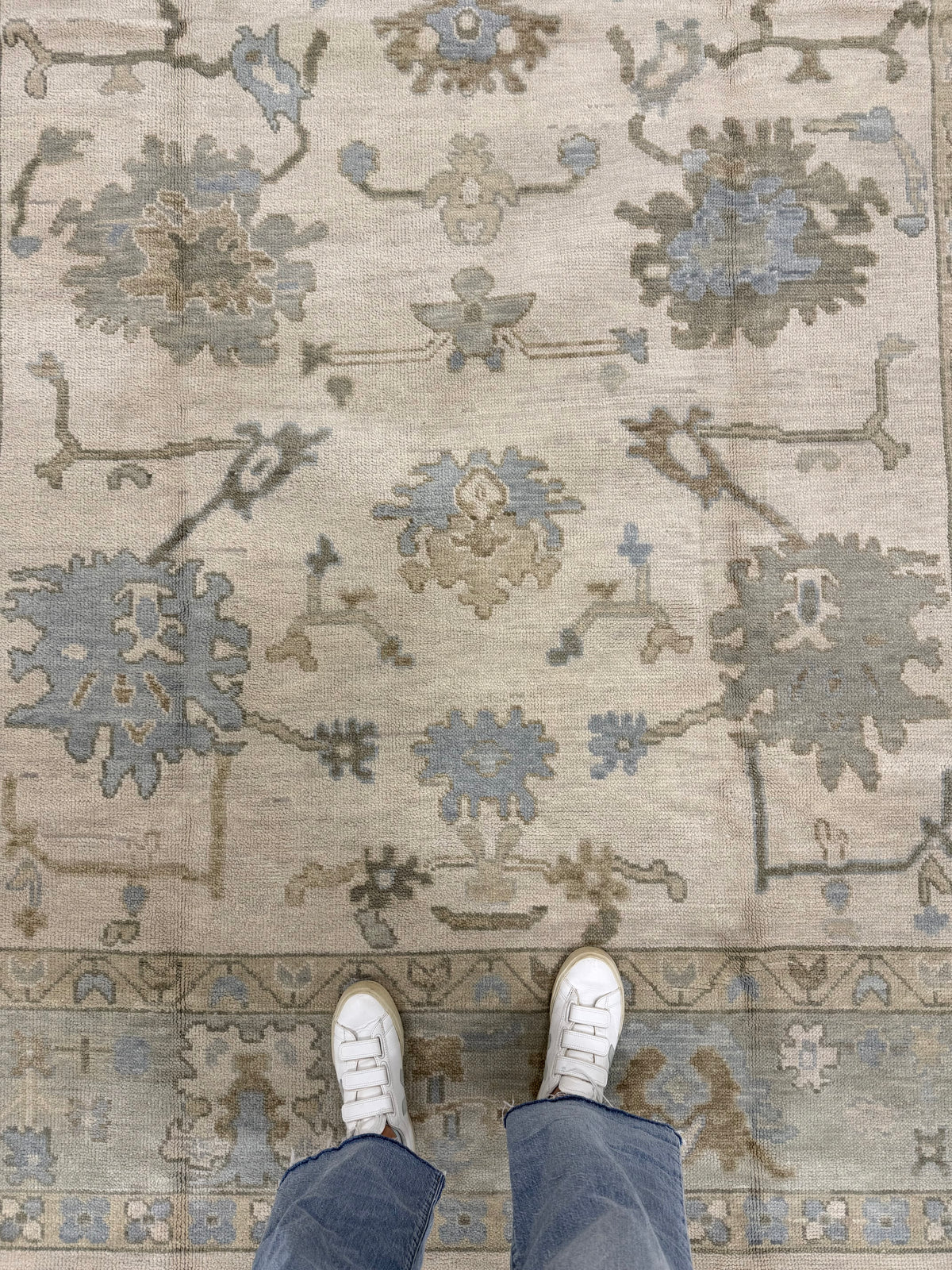 Evangeline Warm Modern Oushak rug, warm tan hand-knotted wool with sage, brown and light blue, with a person standing on it