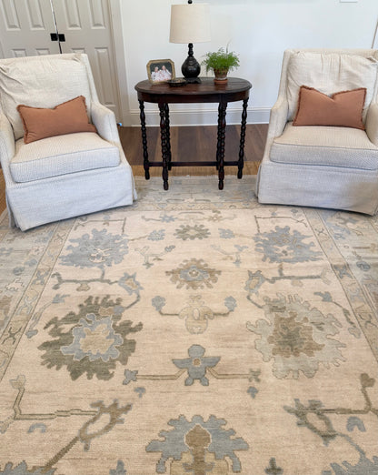 Evangeline warm hand knotted neutral oushak rug in living room with white swivel chairs and antique table