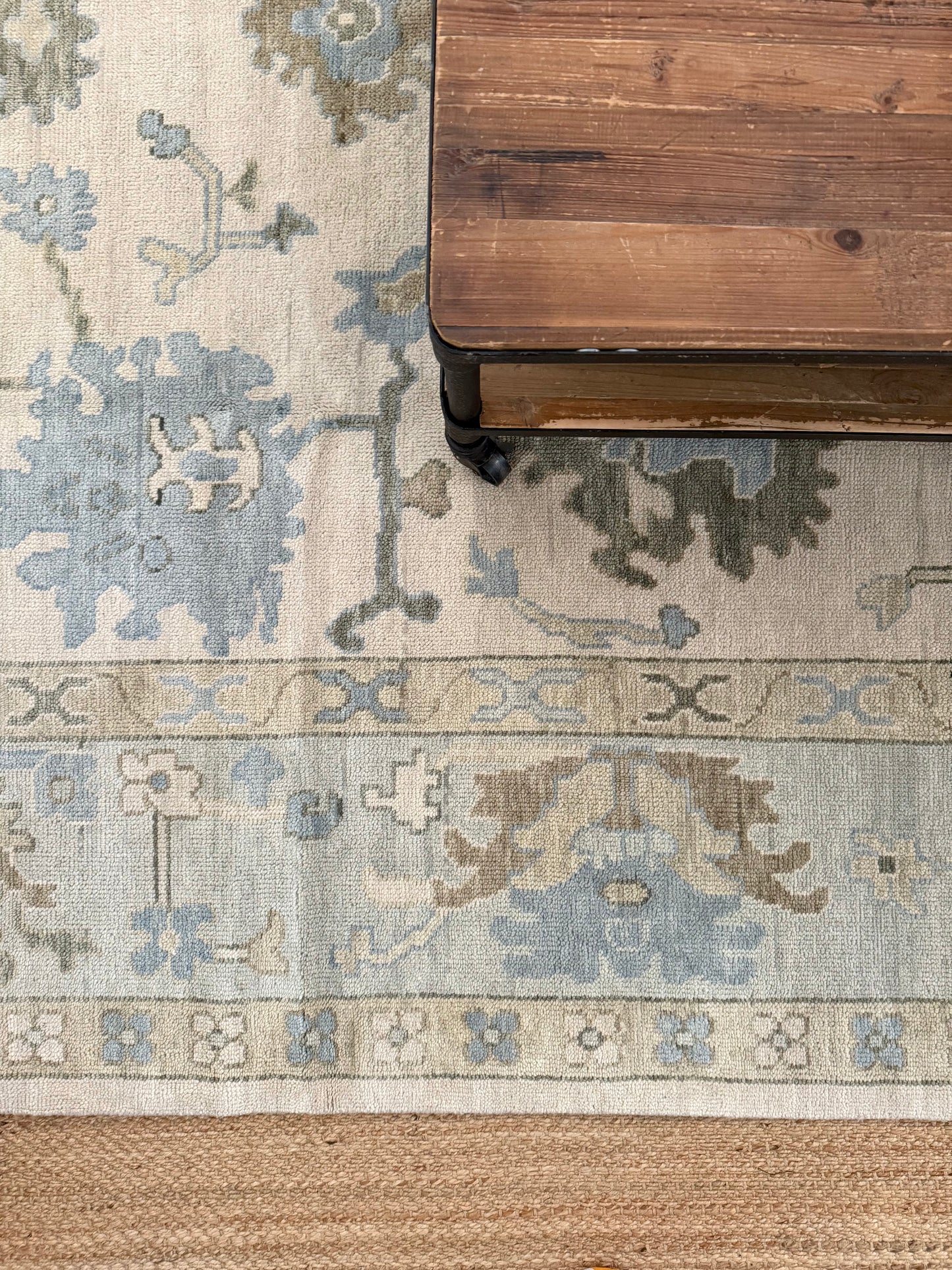 Evangeline warm blue and green oushak rug layered with jute rug and wood table atop