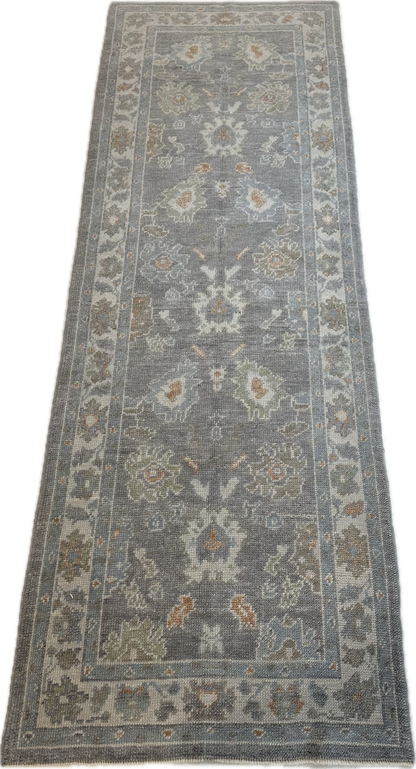 Margaret Turkish Oushak rug, a slate gray foundation, cream border, and light green, pale blue, warm tan, and muted orange accents