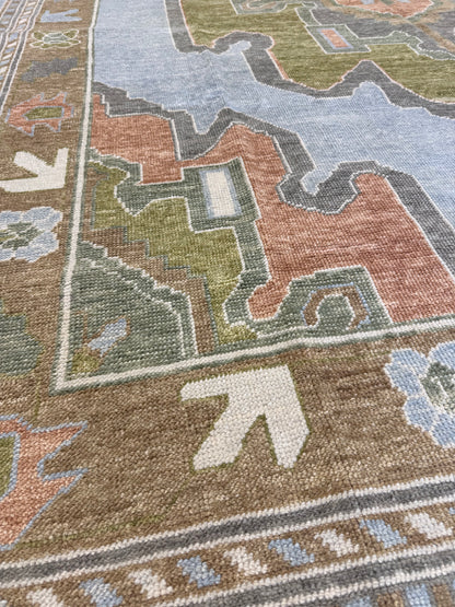 Veda denim blue Turkish Oushak rug with a warm brown border and slate gray, moss green, rust, and brown accents, hand-knotted wool