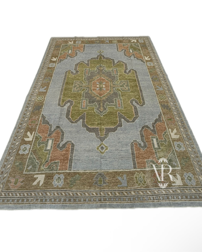 Veda Turkish Oushak rug, hand-knotted wool with a denim blue background, warm brown border, and slate gray, moss green, rust, and soft brown accents