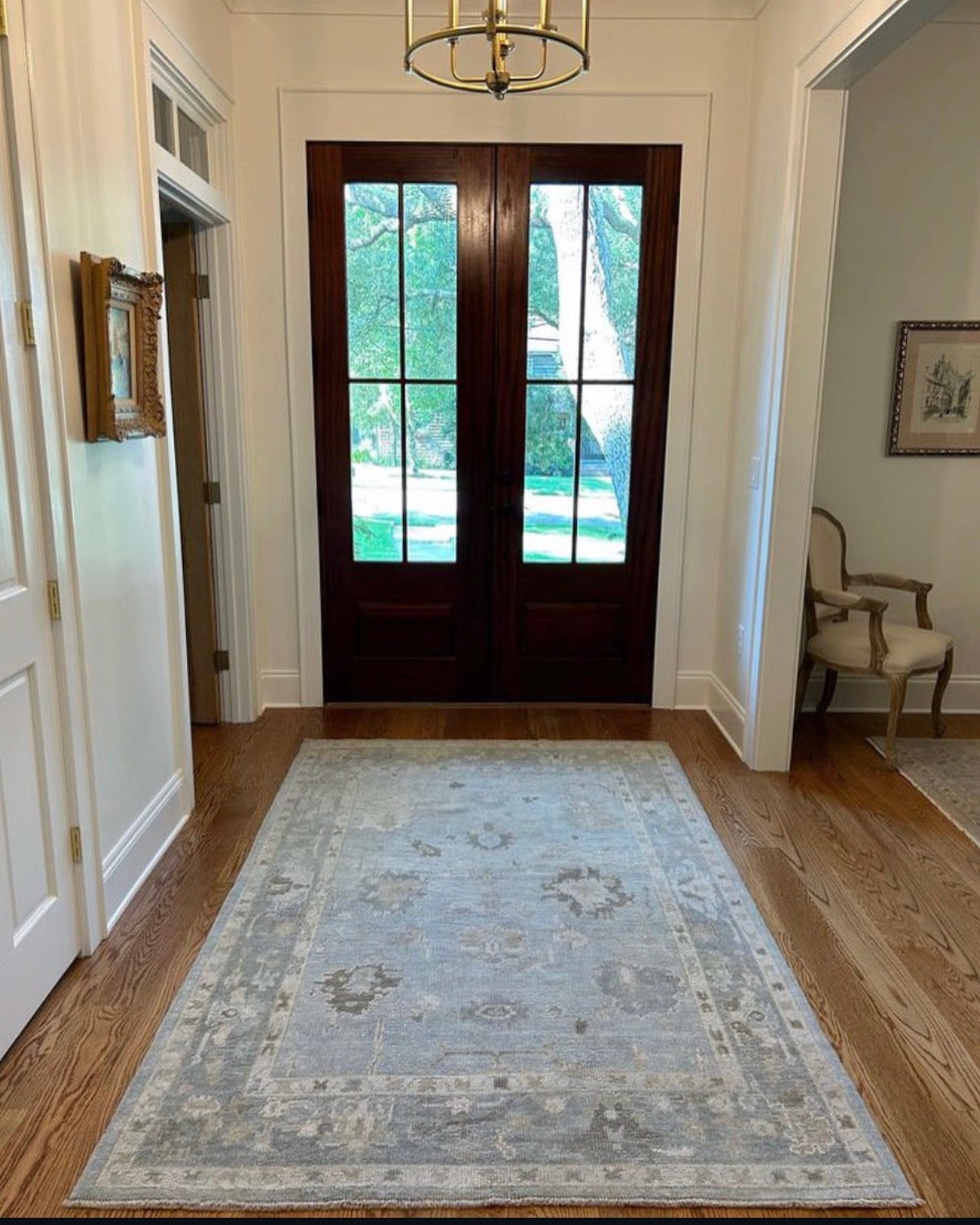 Blue turkish oushak wool rug in foyer entryway with stained doors and wooden floors
