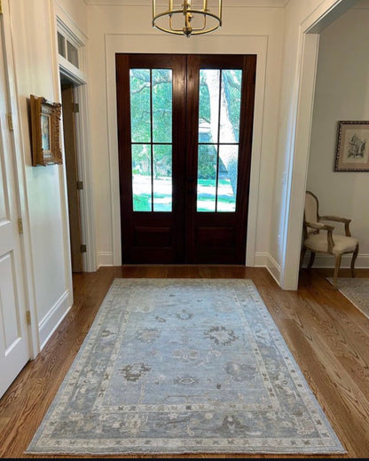 Blue turkish oushak wool rug in foyer entryway with stained doors and wooden floors
