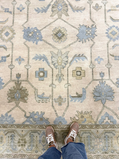 Laurel modern Oushak rug featuring a cream base with a soft seafoam border and accents of green, tan, and dusty blue, hand-knotted wool rug by Vintage Rugs by the Bay being stood on with jeans and brown shoes