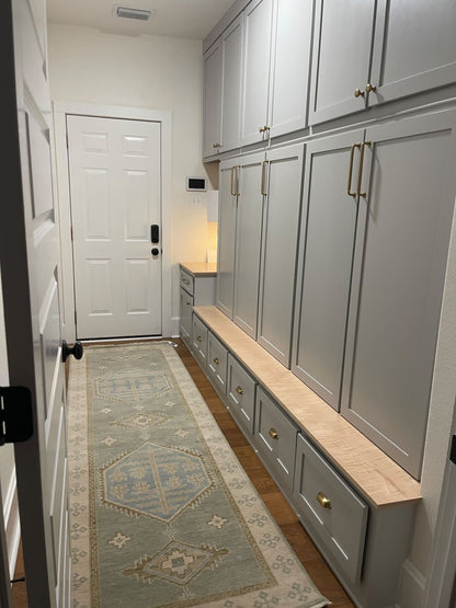 Lennon Blue and green 100% wool Modern Oushak rug with neutral border and green accents and blue center medallion in mudroom with gray-blue cabinets