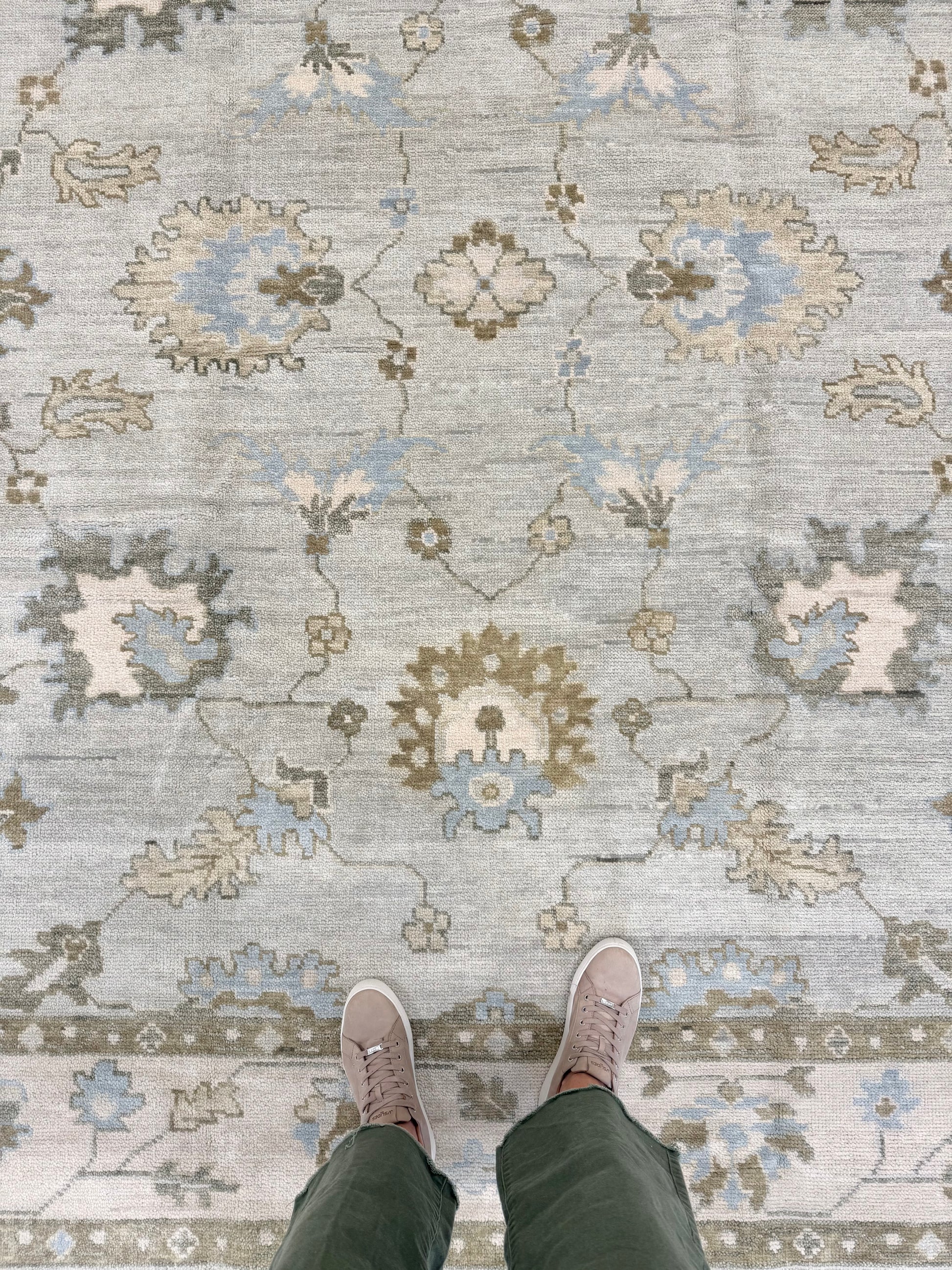 Person wearing mushroom colored shoes standing on a Sage Green Modern Oushak hand-knotted wool rug with blues, greens, creams and browns