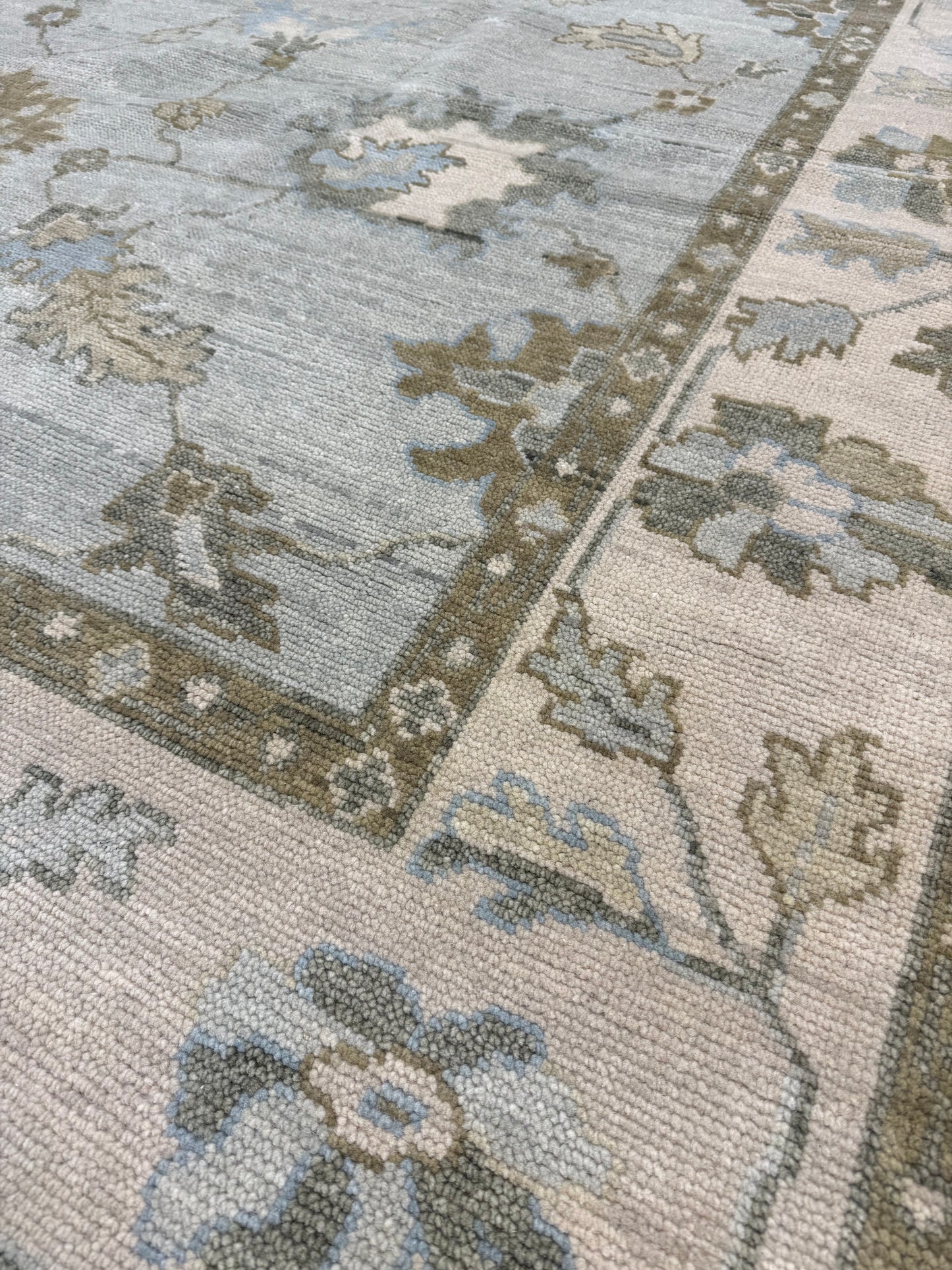 Close up of Sage Green Modern Oushak hand-knotted wool rug with blues, greens, browns, and cream border.