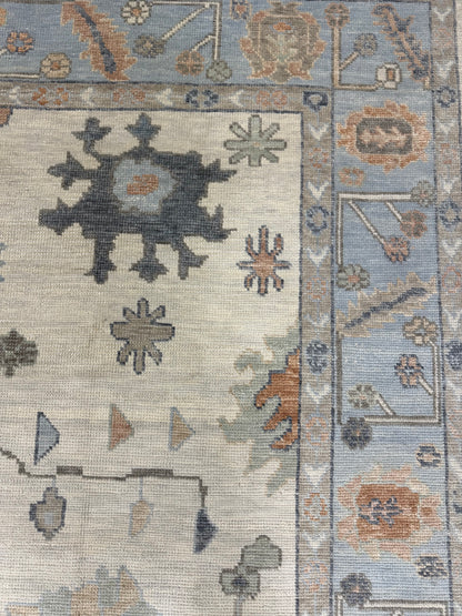 Close-up of a neutral Turkish Oushak rug with geometric designs in blue, brown, orange, coral, and gray.