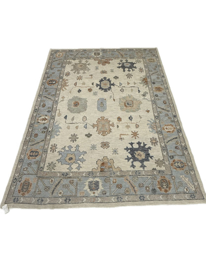Lottie turkish oushak wool rug with cream background, blue border, navy, orange, green, light blue, and coral accents.  