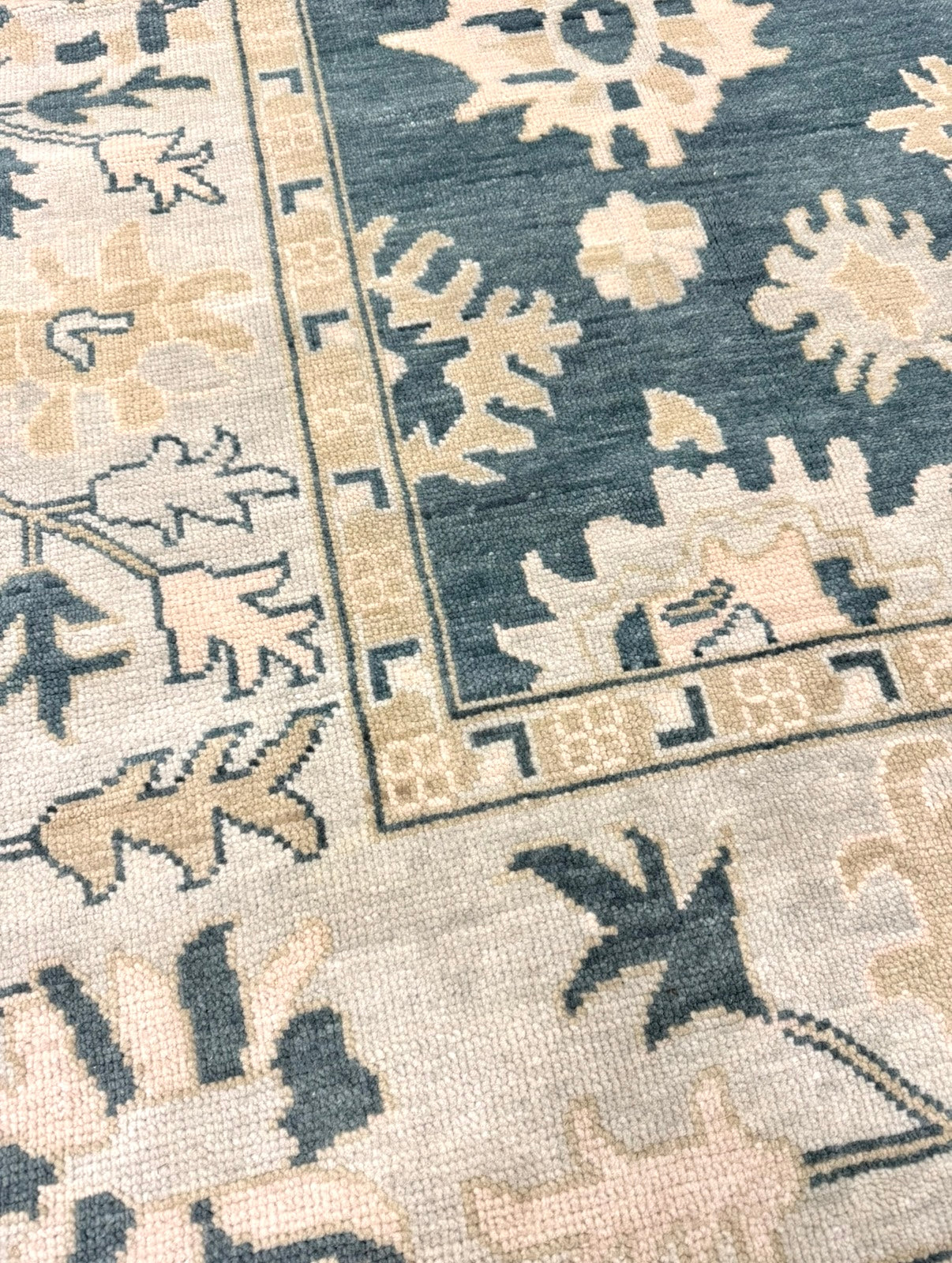 Close up of Lucille modern oushak rug features a dark turquoise base, seafoam border, and cream and tan accents. 
