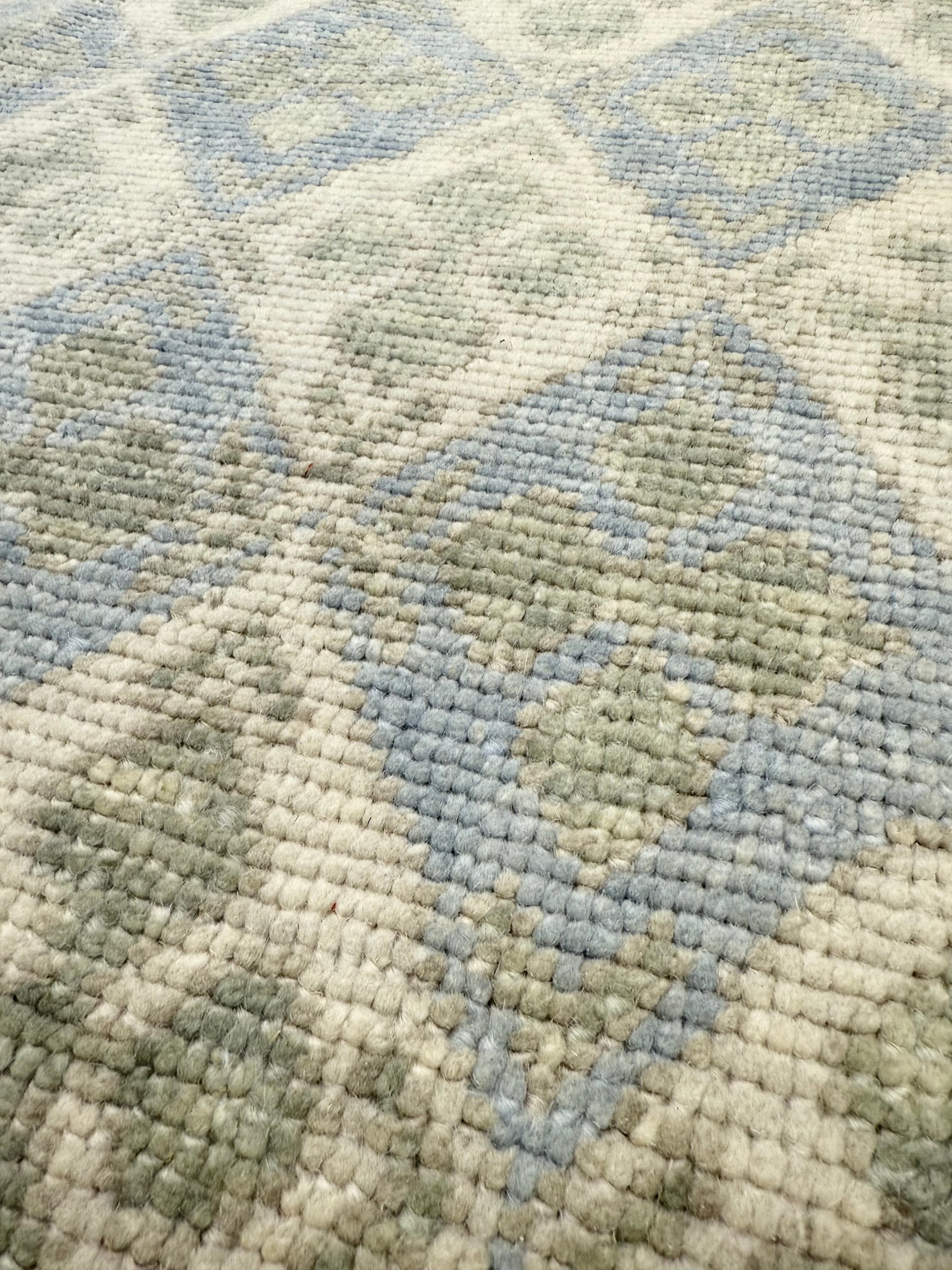 Close-up of hand-knotted turkish Oushak rug with a geometric pattern in shades of blue, green, and beige.
