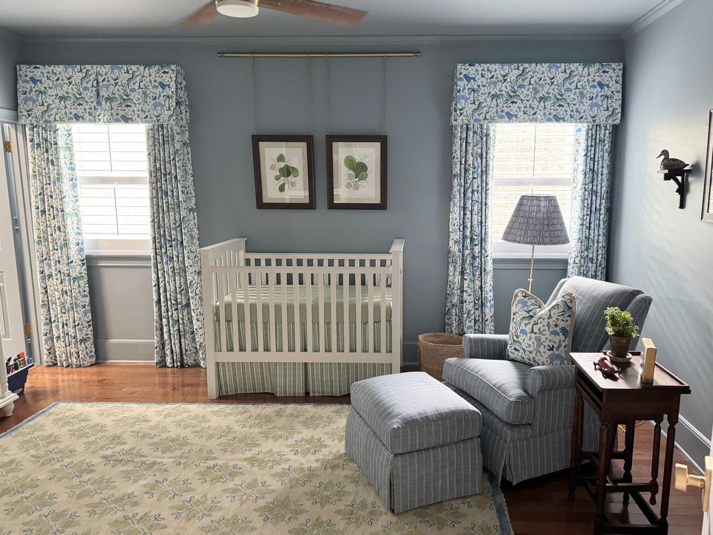 A modern Oushak area rug with a warm gray background and pops of color from cobalt blue, chartreuse, and light coral, displayed in a blue baby nursery with blue chair.