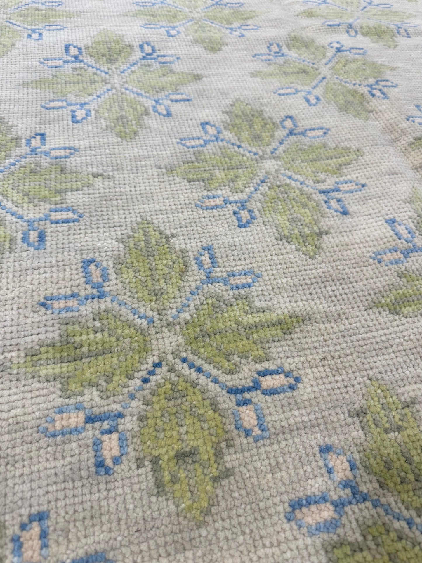 A hand-knotted wool modern Oushak area rug with a warm gray background and pops of color from cobalt blue, chartreuse, and light coral close up.