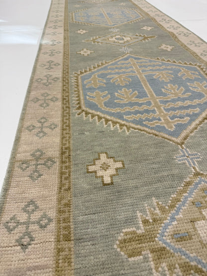 close up of Lennon Blue and green 100% wool Modern Oushak rug with neutral border and green accents and blue center medallion