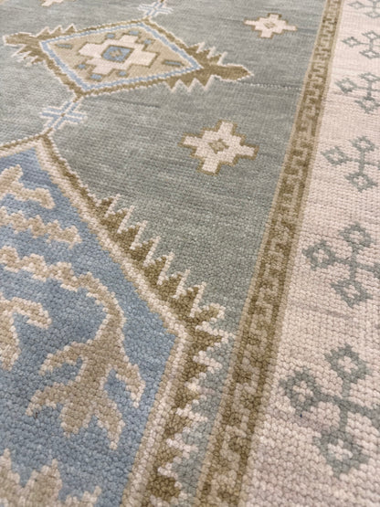 close up of Lennon Blue and green 100% wool Modern Oushak rug with neutral border and green accents and blue center medallion