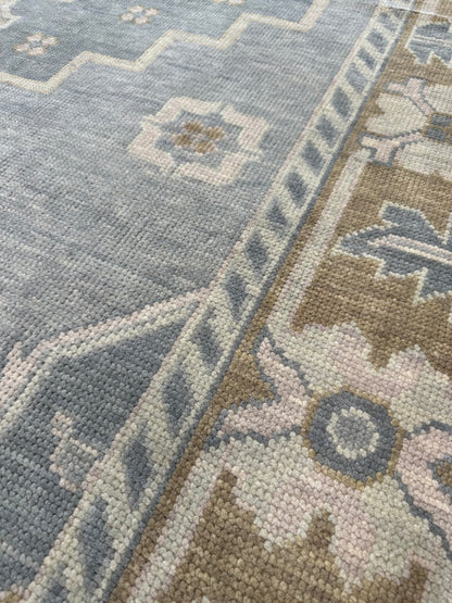 Susie gray-blue modern Oushak rug with a warm brown border and sage green, tan, and cool gray accents, hand-knotted wool