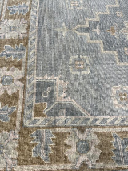 Susie modern Oushak rug, hand-knotted wool with a soft gray-blue base, warm brown border, and sage green, tan, and cool gray accents