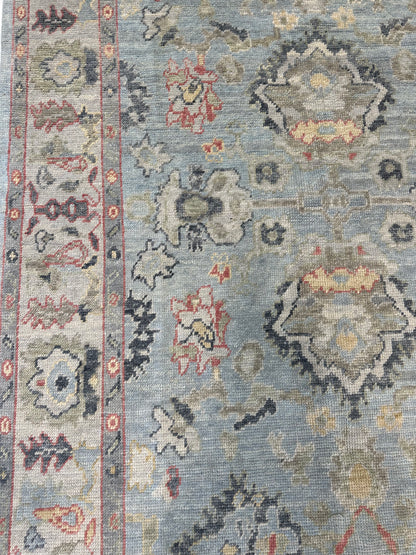 Kennedy hand-knotted wool Turkish Oushak rug in light blue with ivory border and jewel-toned accents