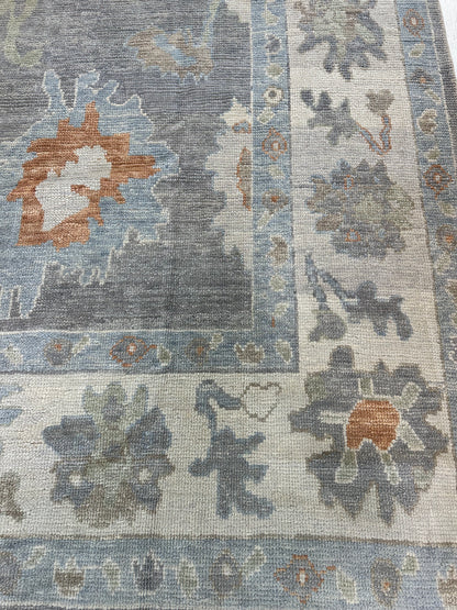 Margaret hand-knotted wool Turkish Oushak rug in a slate gray foundation, cream border, and light green, pale blue, warm tan, and muted orange accents