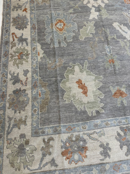 Margaret hand-knotted wool Turkish Oushak rug in a slate gray foundation, cream border, and light green, pale blue, warm tan, and muted orange accents