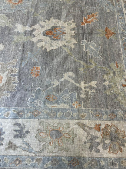 Margaret Turkish Oushak rug with a slate gray foundation, cream border, and light green, pale blue, warm tan, and muted orange accents, hand-knotted wool