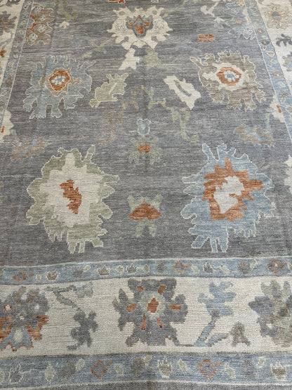 Margaret Turkish Oushak rug, a slate gray foundation, cream border, and light green, pale blue, warm tan, and muted orange accents