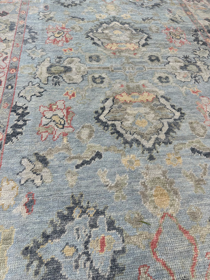 Kennedy hand-knotted wool Turkish Oushak rug in light blue with ivory border and jewel-toned accents