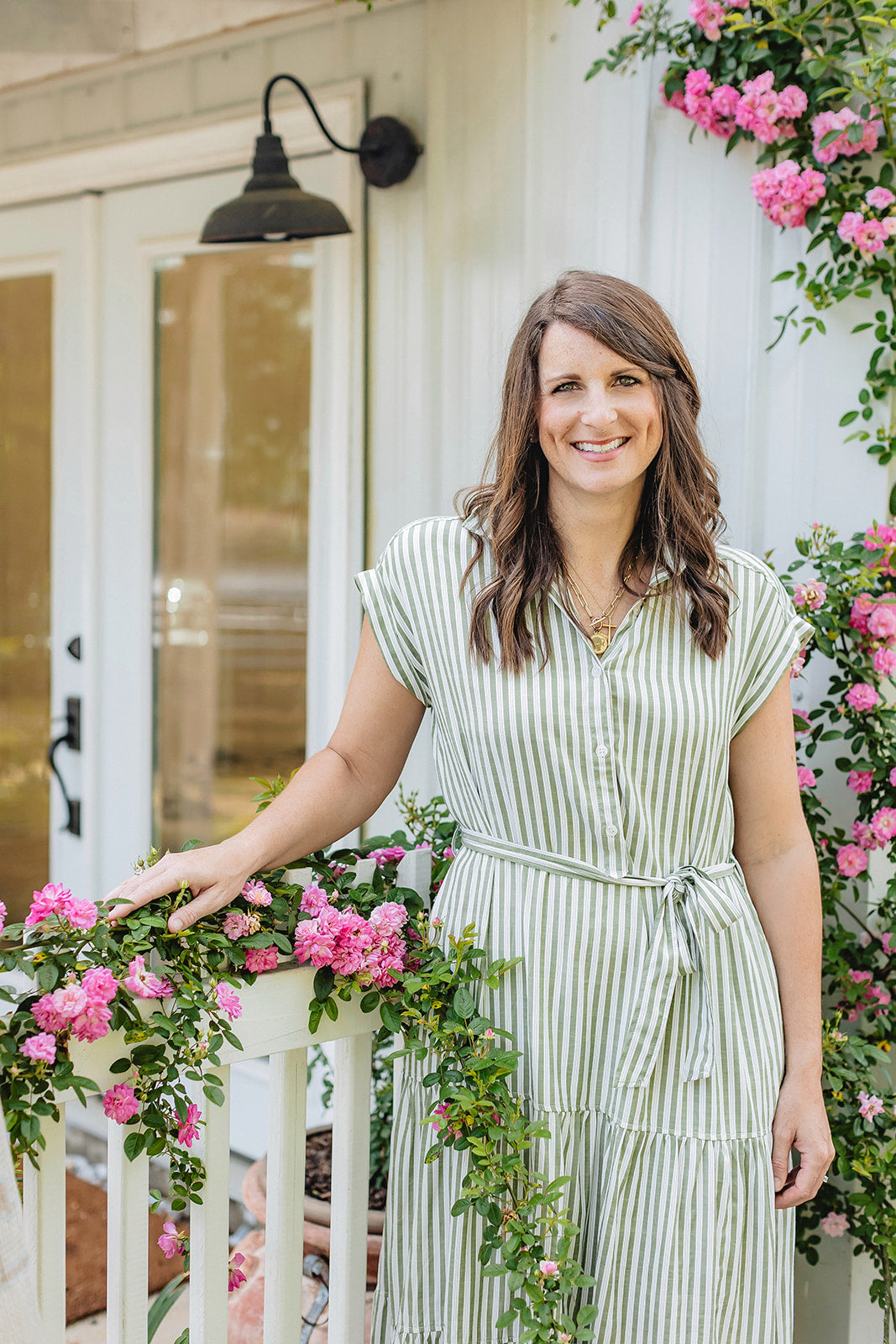 Woman in a striped dress standing in front of a white door with pink flowers.