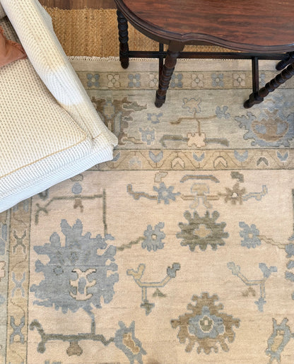 Evangeline warm neutral modern oushak rug with blues and greens with white swivel chair and antique table