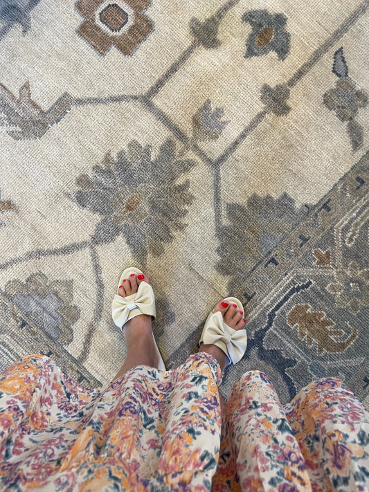 A view of a person's feet wearing floral patterned shoes, standing on a traditional style multicolored area rug with a floral pattern.