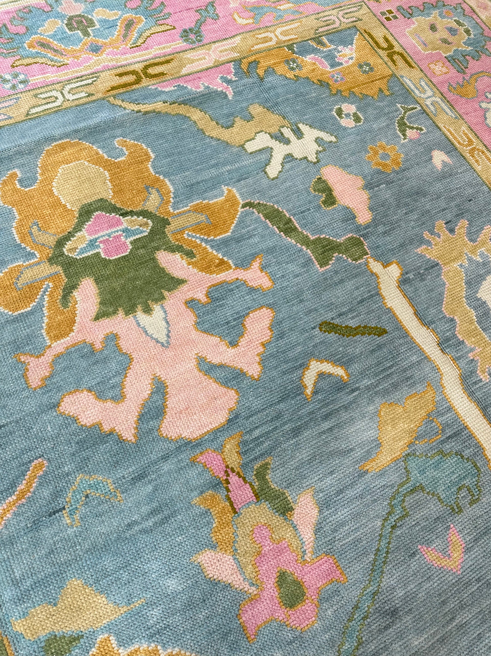 Close-up of Addie Modern Oushak rug showing medium blue, pink border, green, orange, tan, cream, chartreuse-olive, hand-knotted wool