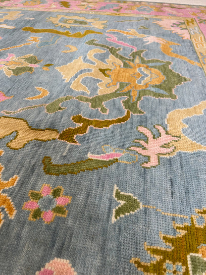 Addie Modern Oushak rug styled in a room, medium blue, pink border, green, orange, tan, cream, chartreuse-olive, hand-knotted wool
